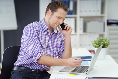 Man in purple and white checkered shirt answering phone calls and starring at laptop